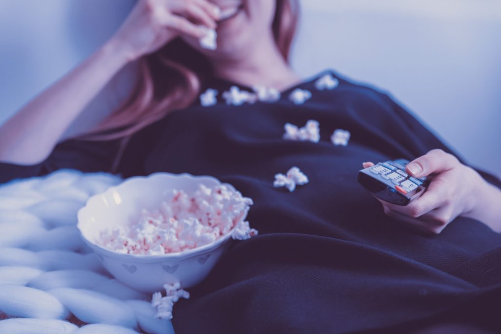 Frau schaut Fernsehen und isst Popcorn.