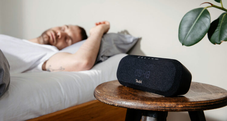 Mann beim Aufwachen im Bett neben einem Radio und einer Pflanze